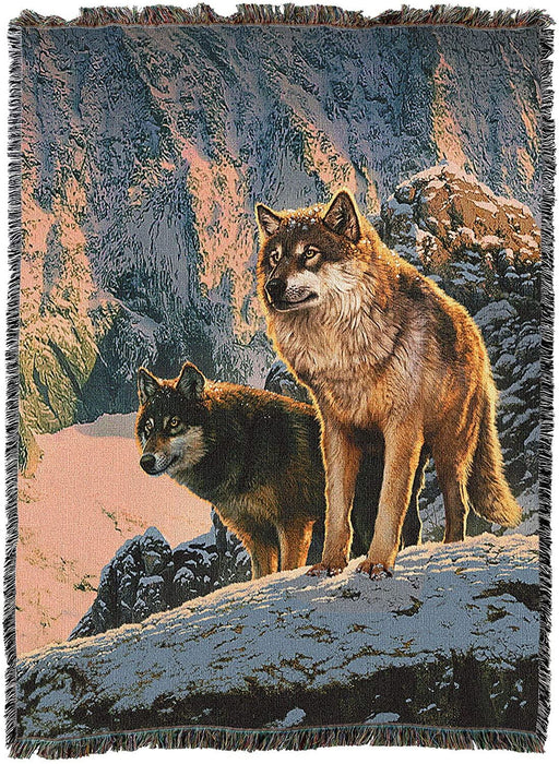 Tapestry blanket showing two wolves standing in the sunset, in a winter mountain landscape.